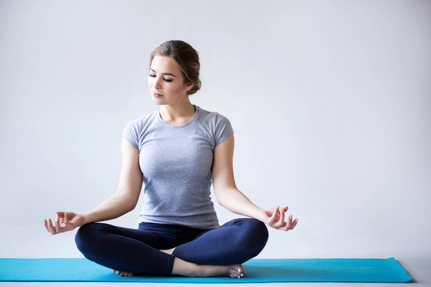 Mulher bonita no sportswear praticando ioga enquanto sentado na posição de lótus no fundo cinza
. - Foto, Imagem