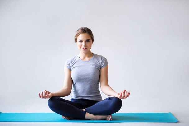 schöne junge Frau in Sportbekleidung praktiziert Yoga, während sie in Lotusposition auf grauem Hintergrund sitzt. - Foto, Bild