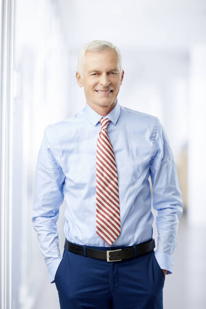 Professional businessman standing at the office while looking at camera and smiling. - Photo, Image