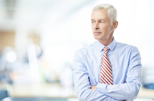 Director financiero senior hombre de negocios mirando reflexivo mientras está de pie en la oficina
. - Foto, imagen