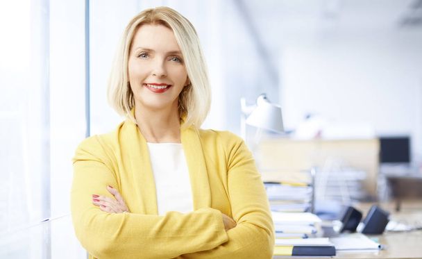 Beautiful mature sales businesswoman wearing casual clothes and smiling while standing with arms crossed at the office.  - Foto, Imagem
