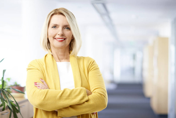Beautiful mature sales businesswoman wearing casual clothes and smiling while standing with arms crossed at the office.  - Foto, immagini