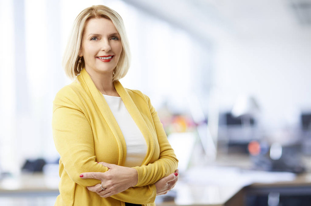 Beautiful mature sales businesswoman wearing casual clothes and smiling while standing with arms crossed at the office.  - Photo, image