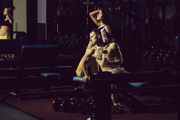 muscular man and sexy girl at gym trainer with bottle - Zdjęcie, obraz