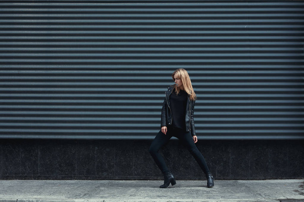 Giovane bella bella bionda ragazza europea passeggiando lungo la strada indossando giacca di pelle nera, jeans neri. Fondo in metallo scuro. Trendy, Urban street style. Autunno stile Vogue. Soffietti tonici
 - Foto, immagini