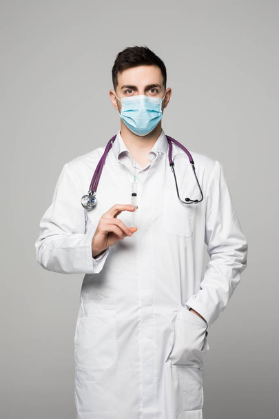 Doctor holds syringe. Man in white coat and surgical mask isolated on white background. - Photo, Image