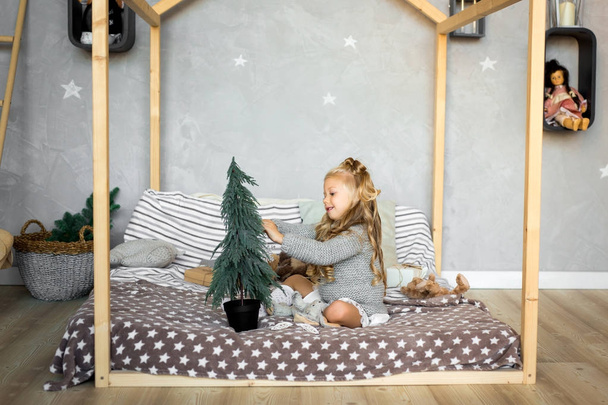 Καλά Χριστούγεννα και καλές γιορτές. Το χαριτωμένο μικρό κορίτσι στολίζει ένα χριστουγεννιάτικο δέντρο. - Φωτογραφία, εικόνα
