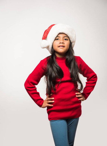 carino poco indiano ragazza indossare Santa cappello e celebrare il Natale mentre in piedi isolato su sfondo bianco - Foto, immagini