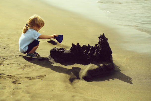 Cute baby boy builds sandcastle on sea beach - Valokuva, kuva