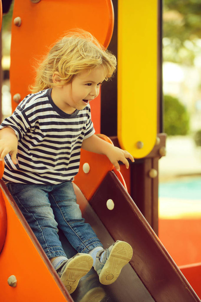 Cute happy baby boy rides from orange slide board - Foto, Imagen