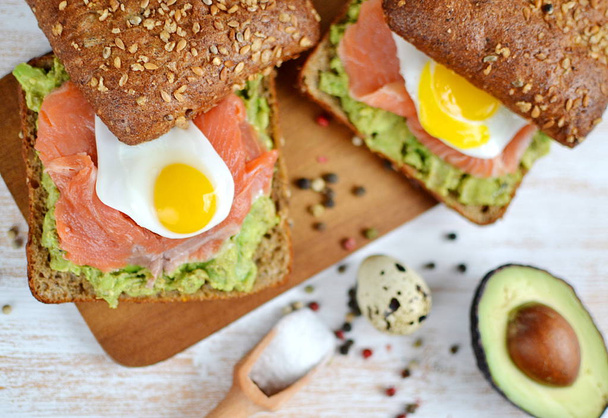 アボカドとウズラ卵食品健康的な朝食の木製の背景とサーモン サンドイッチをスモーク - 写真・画像