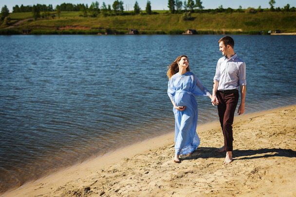 tuleva äiti ja isä kävelemässä hiekalla pitäen toisiaan kädestä
 - Valokuva, kuva