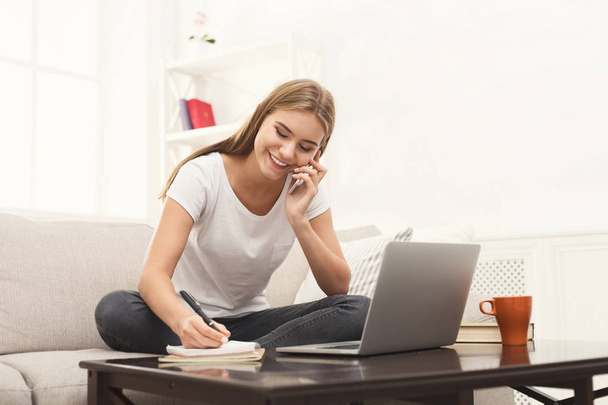 Chica con portátil y móvil sentado en un sofá beige
. - Foto, imagen