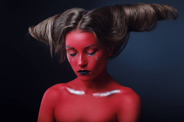 Portrait of a girl in a high fashion, beauty style with red skin, black lips make up at dark background. Devil makeup fashion art design. Halloween holiday concept - Photo, Image