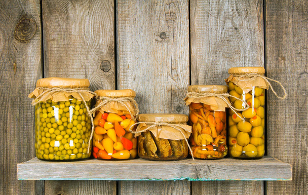 Preserved food in glass jars, on a wooden shelf. - Photo, Image