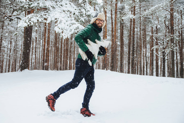 Outdoor Portret van positieve gelukkig man heeft leuke wandelingen in winter bos, geniet van de prachtige landschappen en verse koude weer, houdt van kunstmatige witte firtree, direct in de camera kijkt. Winter concept - Foto, afbeelding