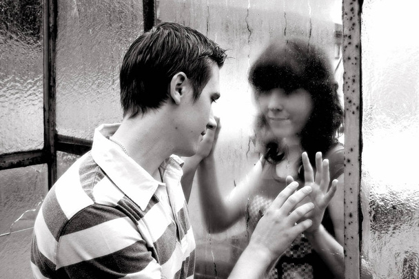 Una joven pareja anhelante está separada por un disco. Una joven pareja se mira a través de un cristal de ventana
 - Foto, imagen
