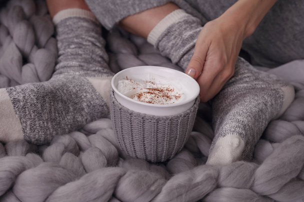 Female feet wearing cozy warm wooleen socks. Warmth concept.Woman covered with warm blanket drinking coffee in bed close up . - Photo, Image