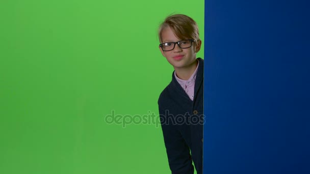 Happy child boy in glasses peeps out from the wall on a green screen - Video, Çekim