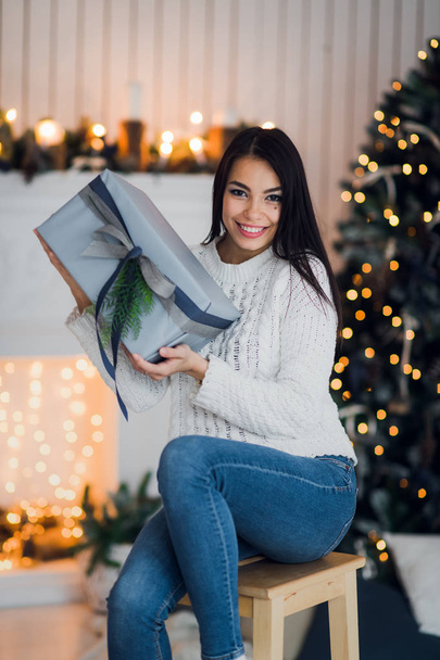 Happy woman Excited To Open Christmas Present sitting at home in front of a christmas tree and fireplace - Fotó, kép
