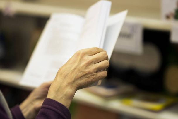 Close-up of hands of the elderly person with open book, bookstore. Real scene. Education concept, Self-study, reading fiction, pension, interests in elderly, life style - Fotografie, Obrázek