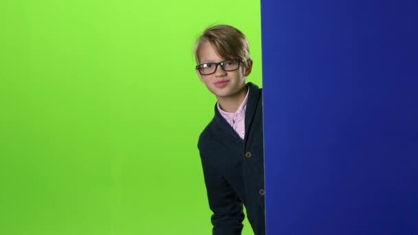 Happy child boy in glasses peeps out from the wall on a green screen. Slow motion - Materiaali, video