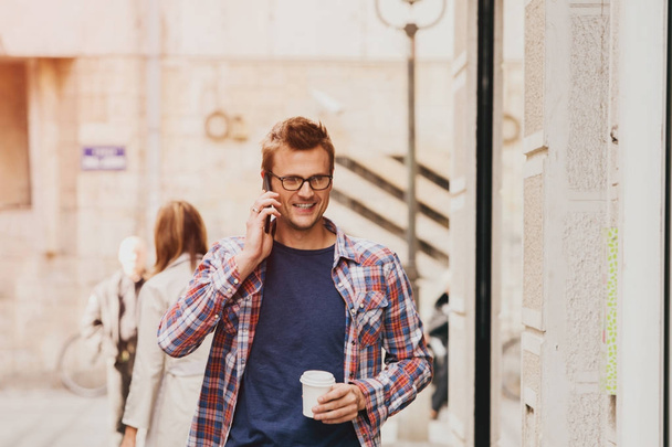 man holding coffee cup and phone, city environment - Photo, image