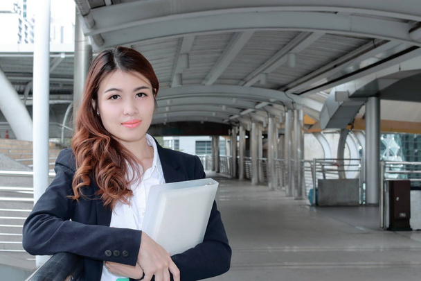 Portrait of confident young Asian business woman standing and holding document folder in her hands at walkway against copy space background. - Photo, Image