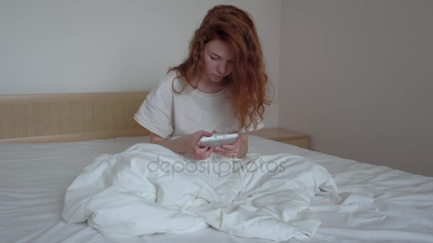 Good looking red-hairs girl with a digital tablet in her bedroom - Imágenes, Vídeo