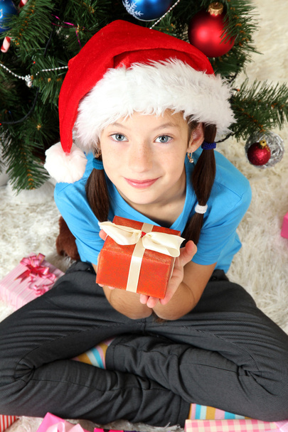 Little girl holding gift box near christmas tree - Foto, Imagen