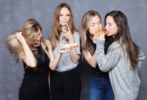 Funny happy shot of young international female students having photo session at gray wall background. Cheerful ladies dancing and enjoying sweets, don't care about their shape. Body positive concept. - Photo, image