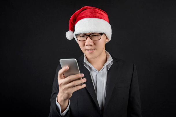 Jeune homme d'affaires asiatique avec chapeau santa en utilisant un smartphone
 - Photo, image