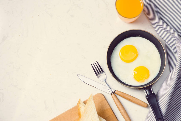 смажені яйця на сковороді, тости та апельсиновий сік на сніданок на білому тлі. Денне світло
. - Фото, зображення