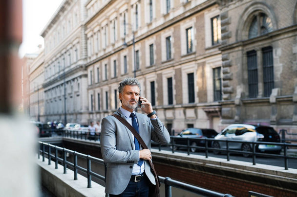 Mature businessman with smartphone in a city. - Zdjęcie, obraz
