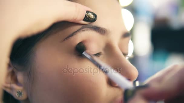 Closeup view of professional makeup artist hands using makeup brush to apply eye shadows. Pro visagiste puts light brown shadows on eyelid of a model. Slowmotion shot - Metraje, vídeo