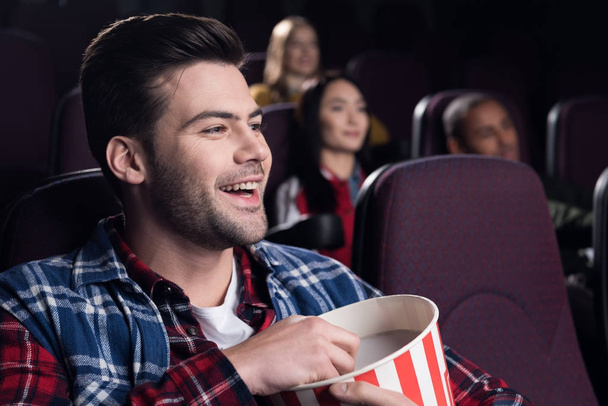 smiling handsome man with popcorn watching movie in cinema - Foto, Imagen