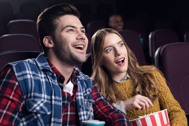Jong paar glimlachend met popcorn kijken naar film in de bioscoop - Foto, afbeelding