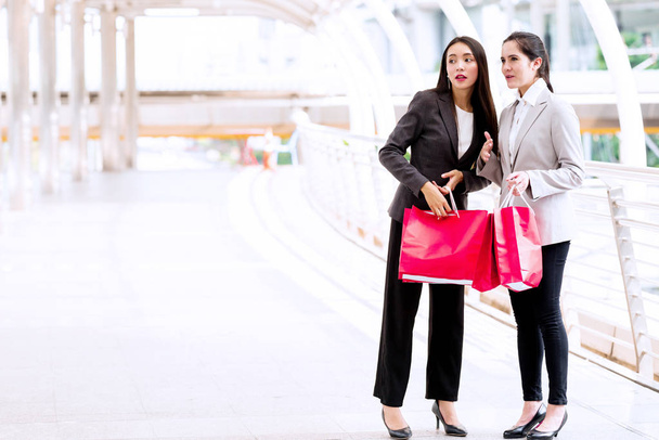 Two beautiful girls shopping together. Asian woman and white girl smartly dress going out shopping during lunch time in work days. Taken outdoor with natural lights in business district walk way. - Фото, зображення