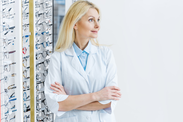 female ophthalmologist standing in optics with glasses on shelves - Photo, Image