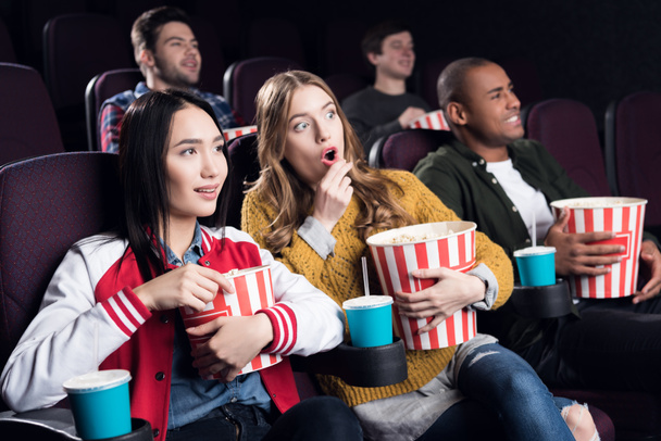 emotional friends with popcorn and soda watching movie in cinema - Photo, Image