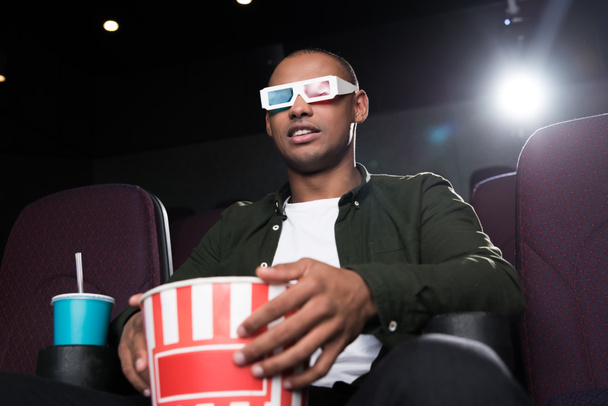 african american man in 3d glasses eating popcorn and watching film in cinema - Fotó, kép
