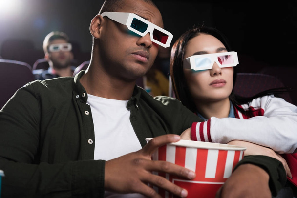 young interracial couple in 3d glasses with popcorn watching movie in cinema - Foto, Imagem