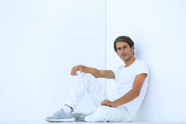 sad young man sitting beside a white wall - Zdjęcie, obraz