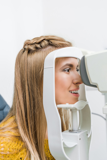 χαμογελώντας ασθενή εξετάζοντας τα μάτια της με σχισμοειδή λυχνία σε κλινική - Φωτογραφία, εικόνα