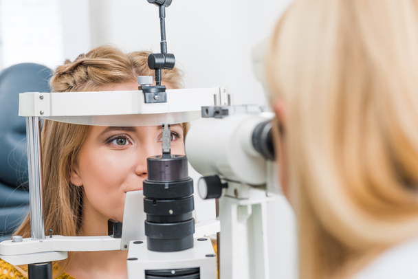 Optometrista femenina examinando paciente a través de lámpara de hendidura en clínica
 - Foto, Imagen