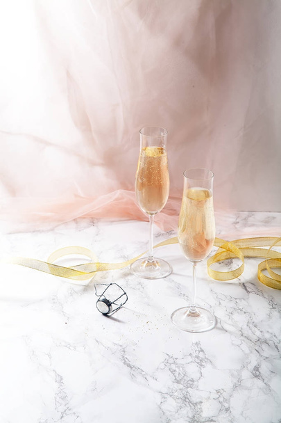 Two flute glasses with champagne on marble background. Pink transparent fabric. Soft light - 写真・画像