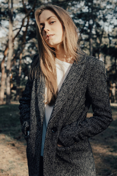 Selbstbewusstes Mode-Model mit langen blonden Haaren blickt im Park in die Kamera - Foto, Bild