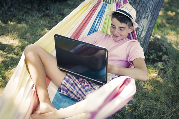 дитина з ноутбуком в гамаку в сутінках літа грає або навчається
 - Фото, зображення