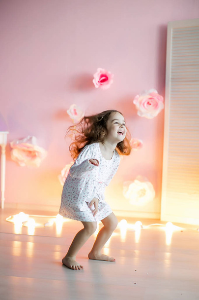 glückliches kleines Mädchen posiert in dekorierten Raum mit Lichtern auf dem Hintergrund - Foto, Bild