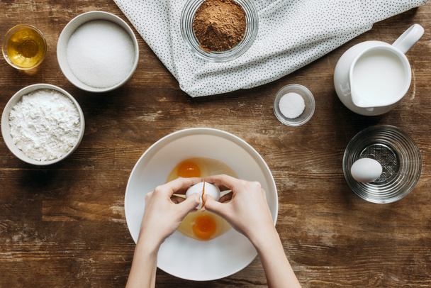 cropped shot of woman breaking eggs into bowl for pastry on wooden table - Photo, Image
